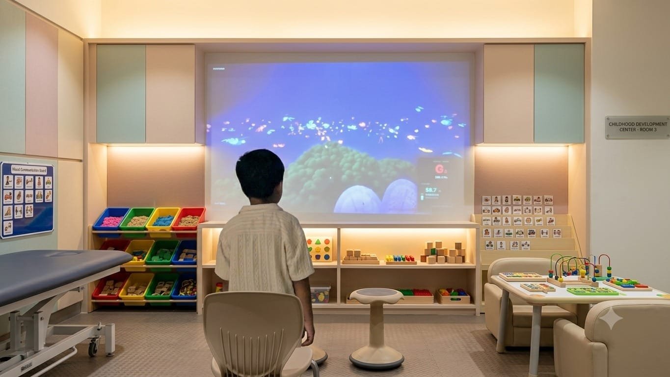 A child seated in front of a projected speech activity in a therapy room